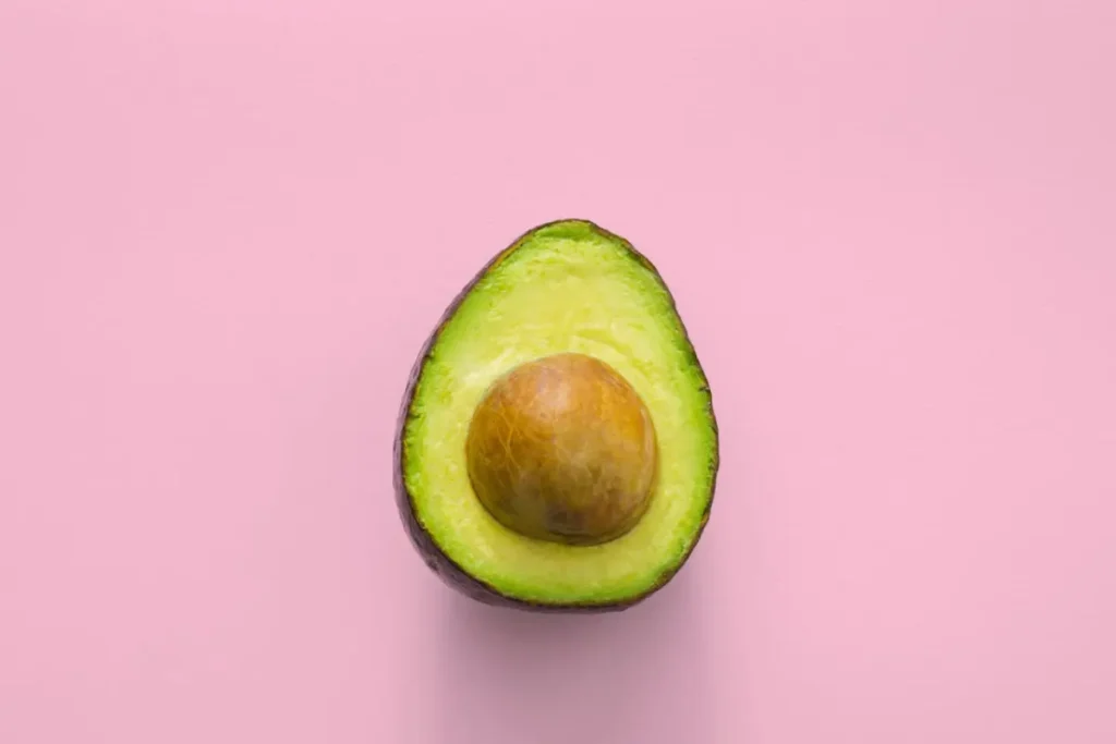 Aguacate cortado a la mitad sobre un fondo rosa