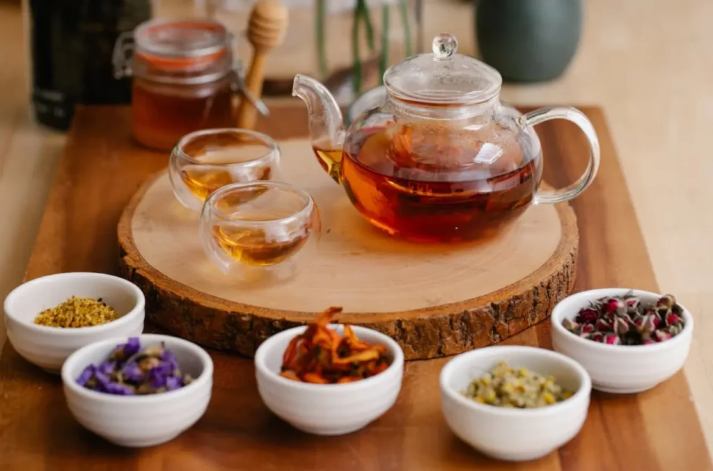 Infusión en una tetera con dos vasos de vidrio y unas tazas con diversas hierbas